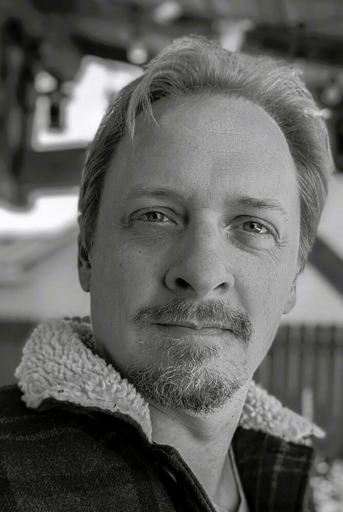 Christopher Brown - narrator B&W photo of a man with piercing eyes, a manly beard and hair that covers the entire top of his head no problem